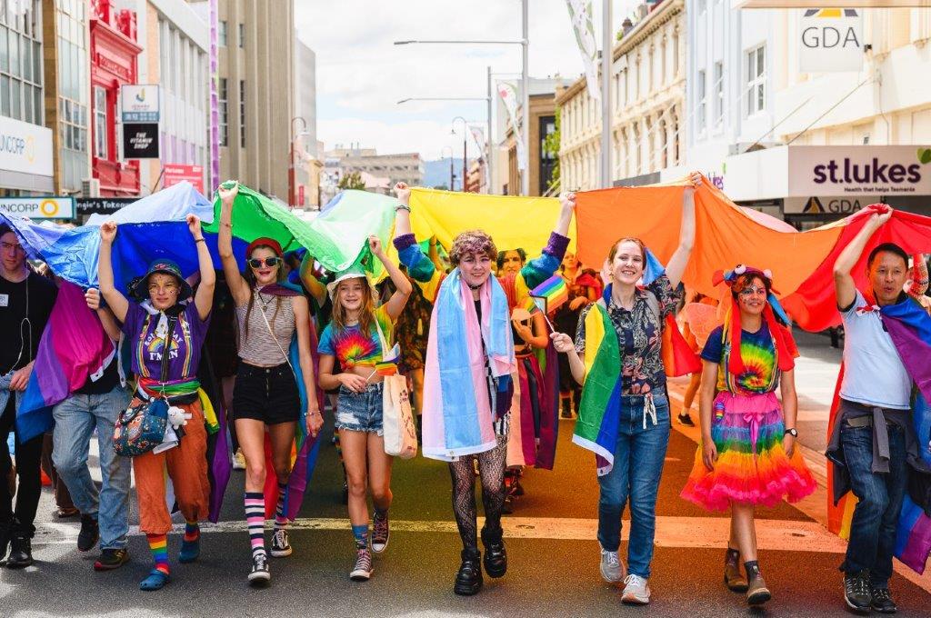 A large group of people holding rainbow coloured flags marching the streets.items