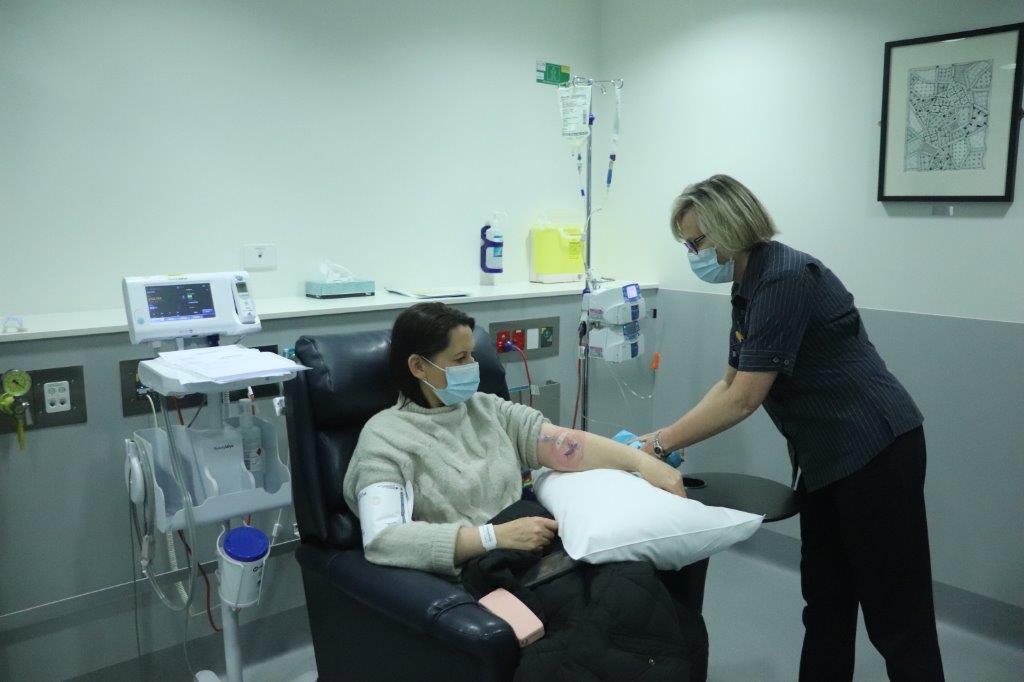 A patient sits in a chair while a nurse takes some blood.